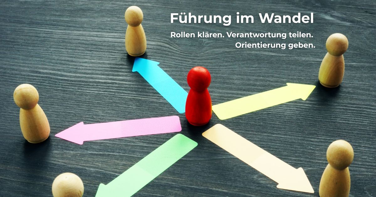 Symbolbild für moderne Führung: Eine zentrale rote Spielfigur mit bunten Pfeilen in Richtung von sechs Holzfiguren, die für verteilte Verantwortung, Orientierung und Kommunikation in digitalen Arbeitsumgebungen steht.