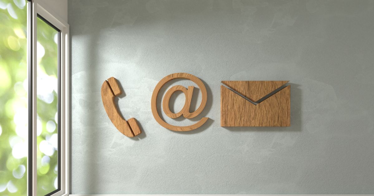 Holzsymbole für Telefon, E-Mail und Kontakt auf heller Wand – visuelle Darstellung moderner Kommunikationswege.